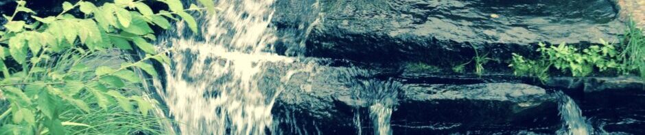 A small waterfall cascading over rocks surrounded by greenery.